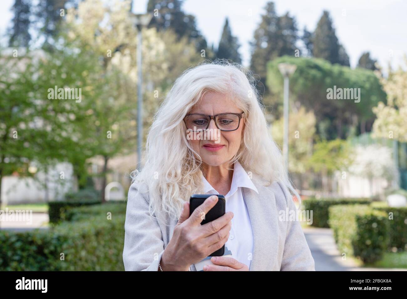 Reife Frau mit langen weißen Haaren mit Mobiltelefon an parken Stockfoto