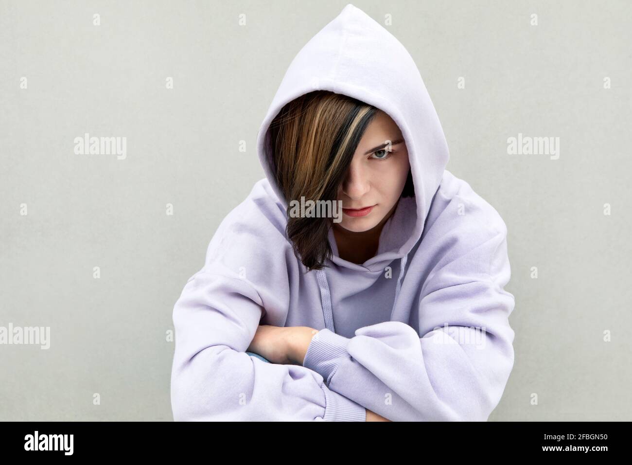 Serious Mädchen mit hervorgehobenen Haaren starrte durch graue Wand Stockfoto