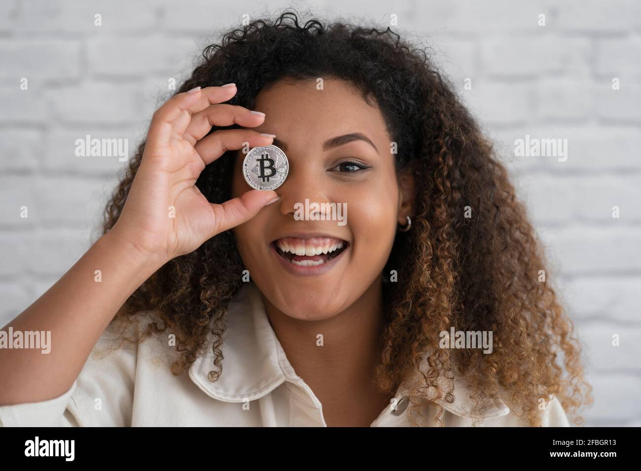 Lächelnde Frau, die die Augen mit silberner Kryptowährung bedeckt Stockfoto