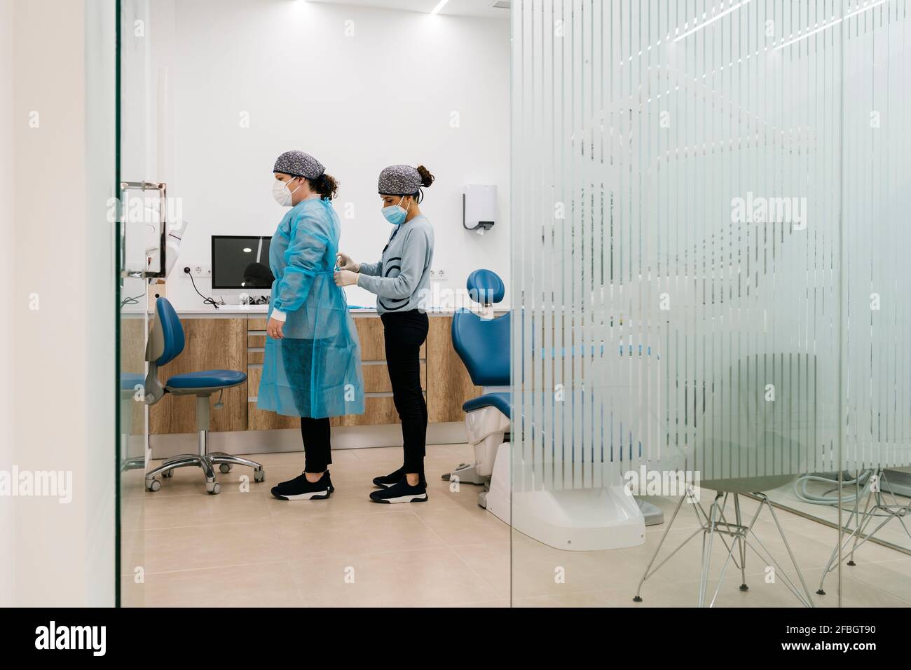 Assistentin hilft dem Arzt, sich in der Klinik in Schutzkleidung anzuziehen Während der COVID-19 Stockfoto