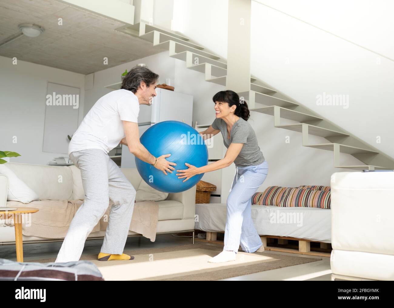 Spielerisches reifes Paar hält den Fitnessball, während es im Leben steht Zimmer zu Hause Stockfoto