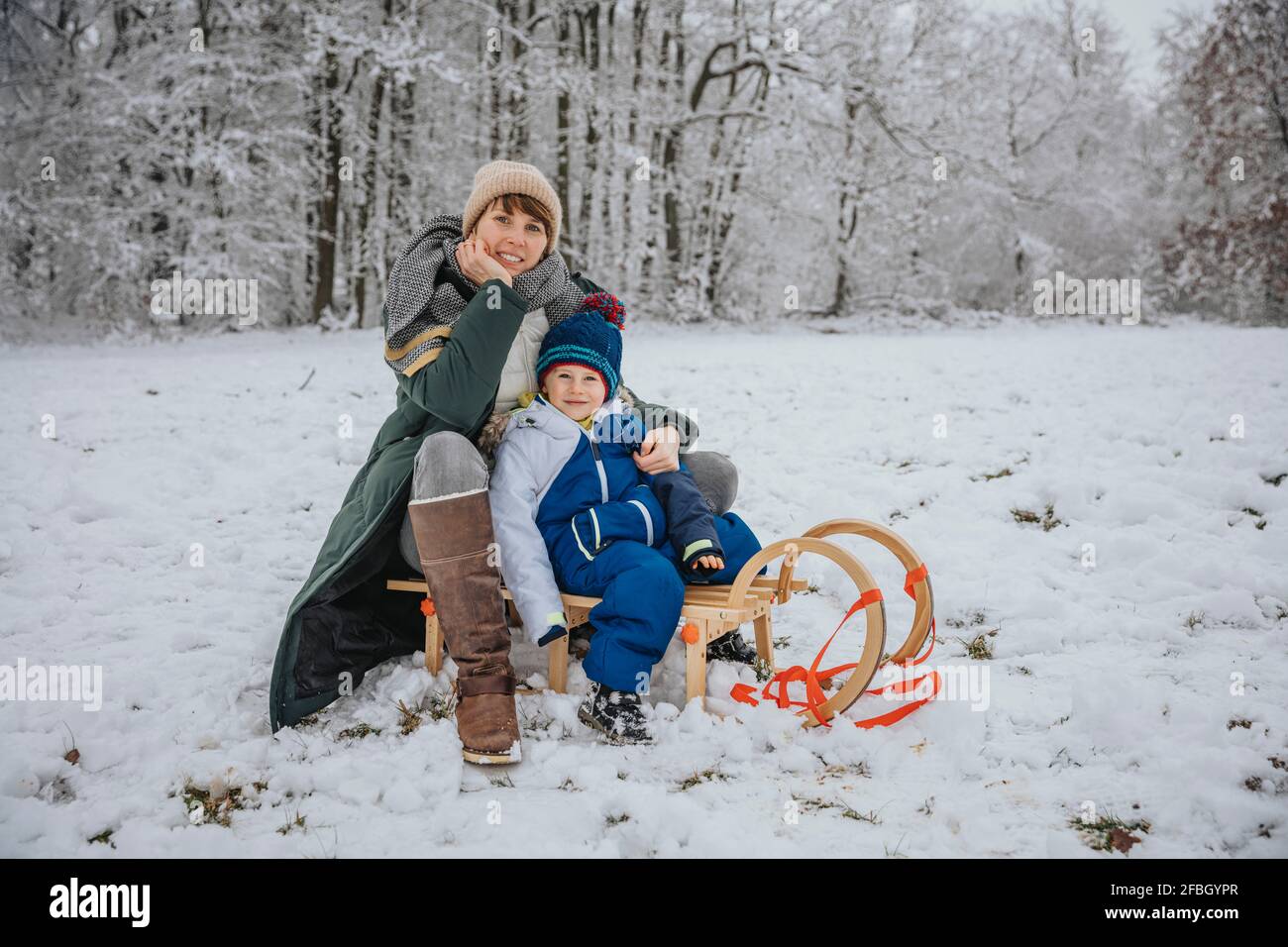 Mutter und Sohn sitzen auf Schlitten auf schneebedecktem Feld während Winter Stockfoto