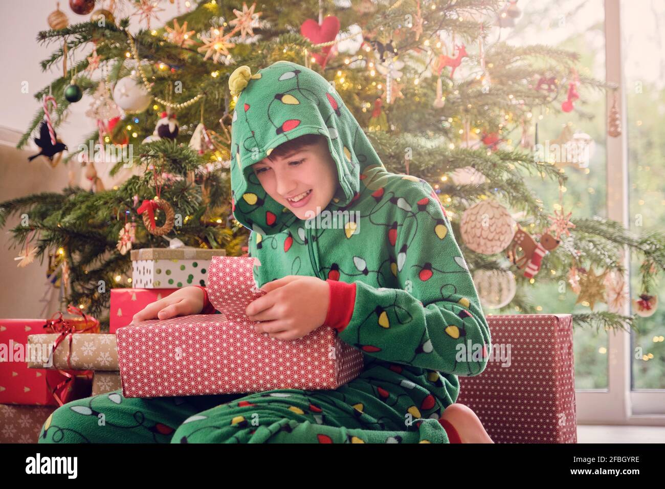Aufgeregt Junge in Kapuze Strampler zerreißenden Wrapper des Geschenks an Zu Weihnachten zu Hause Stockfoto