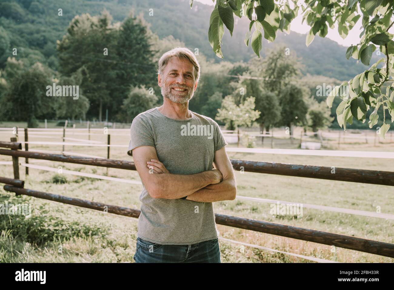 Lächelnder reifer Mann mit gekreuzten Armen, die am Geländer stehen Stockfoto