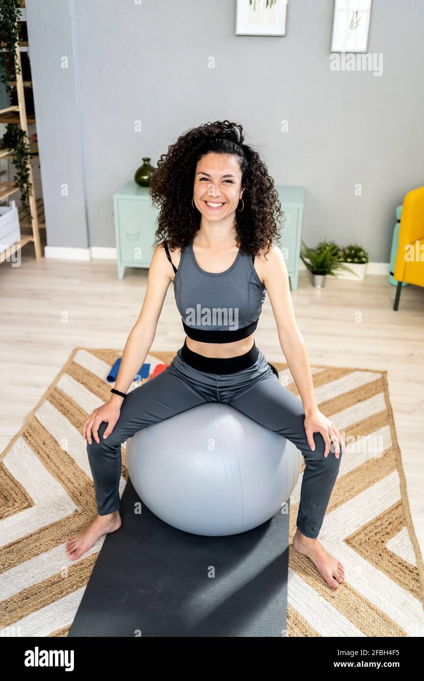 Glückliche Frau, die im Wohnzimmer auf dem Fitnessball sitzt Stockfoto