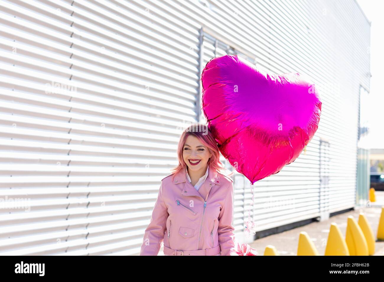 Lächelnder Mann mit glänzendem rosa Ballon, der bei Sonnenschein wegschaut Tag Stockfoto