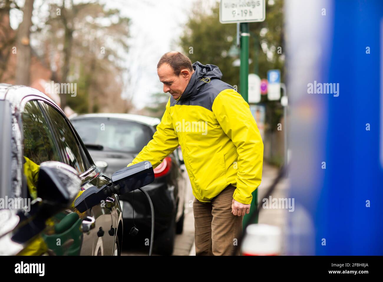Mann lädt Elektroauto mit Stromkabel an der Ladestation Stockfoto