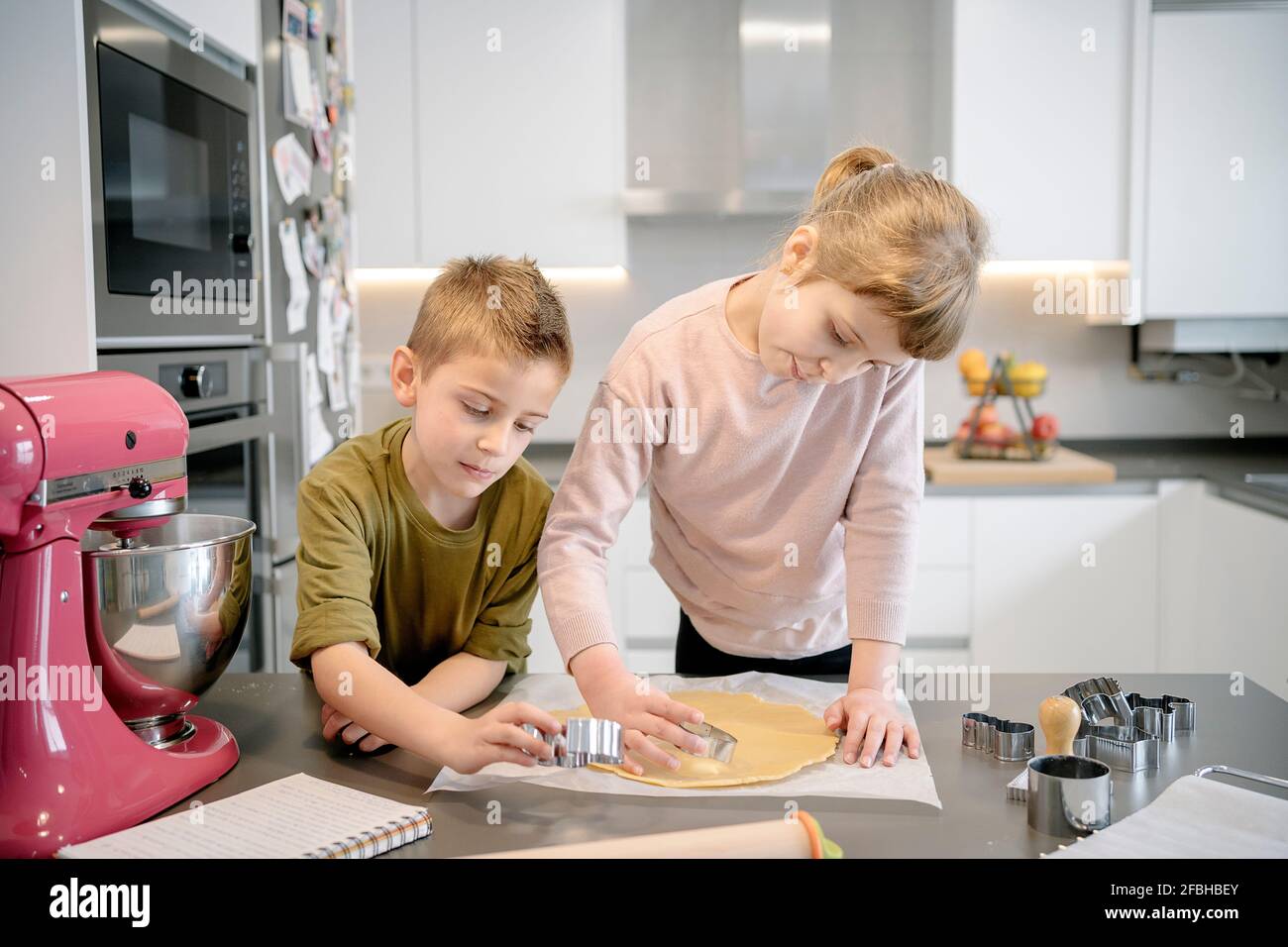 Mädchen und Jungen mit Ausstechform auf Teig in der Küche Stockfoto