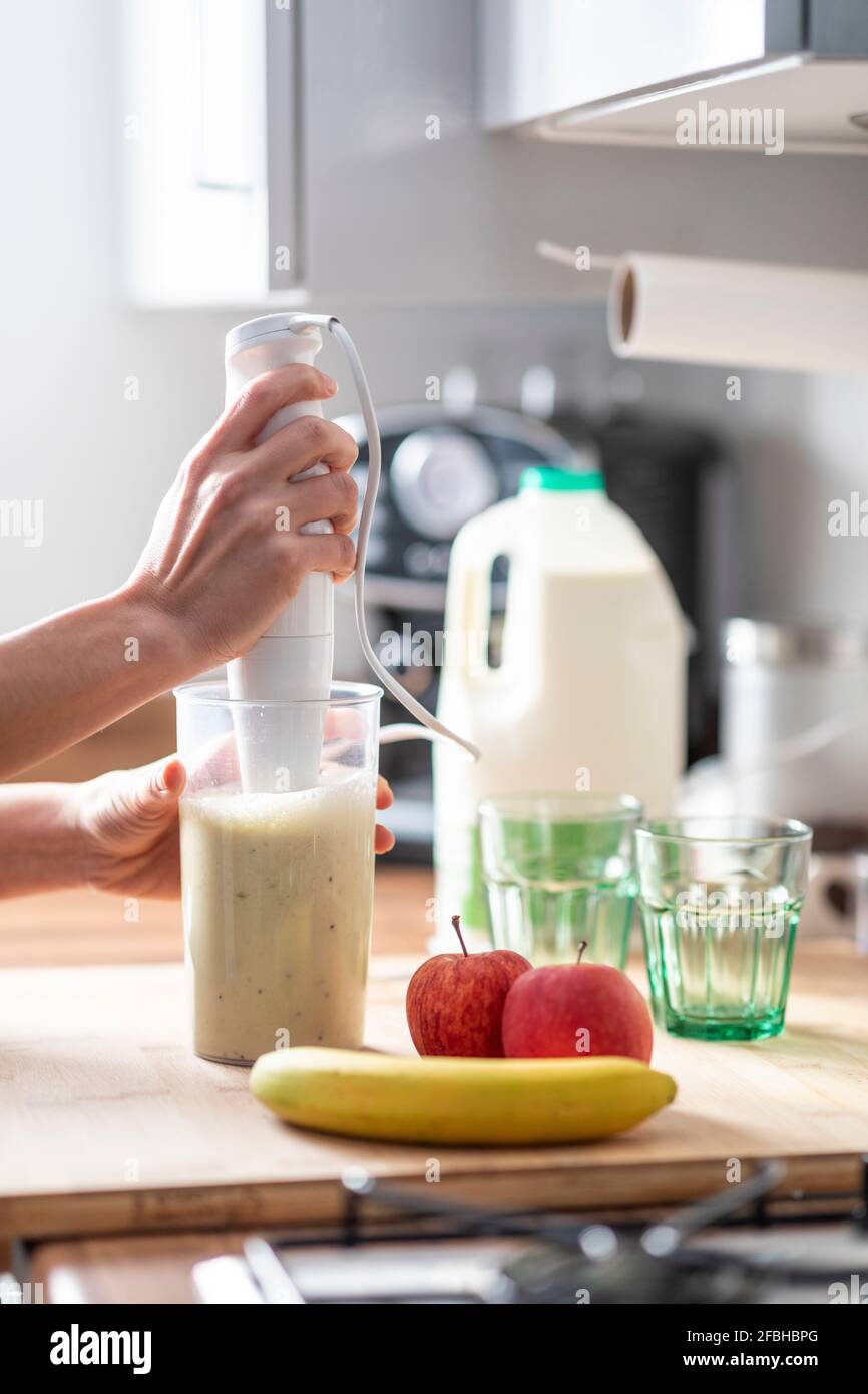 Frau bereitet zu Hause mit einem elektrischen Mixer Fruchtmilchshake zu Stockfoto