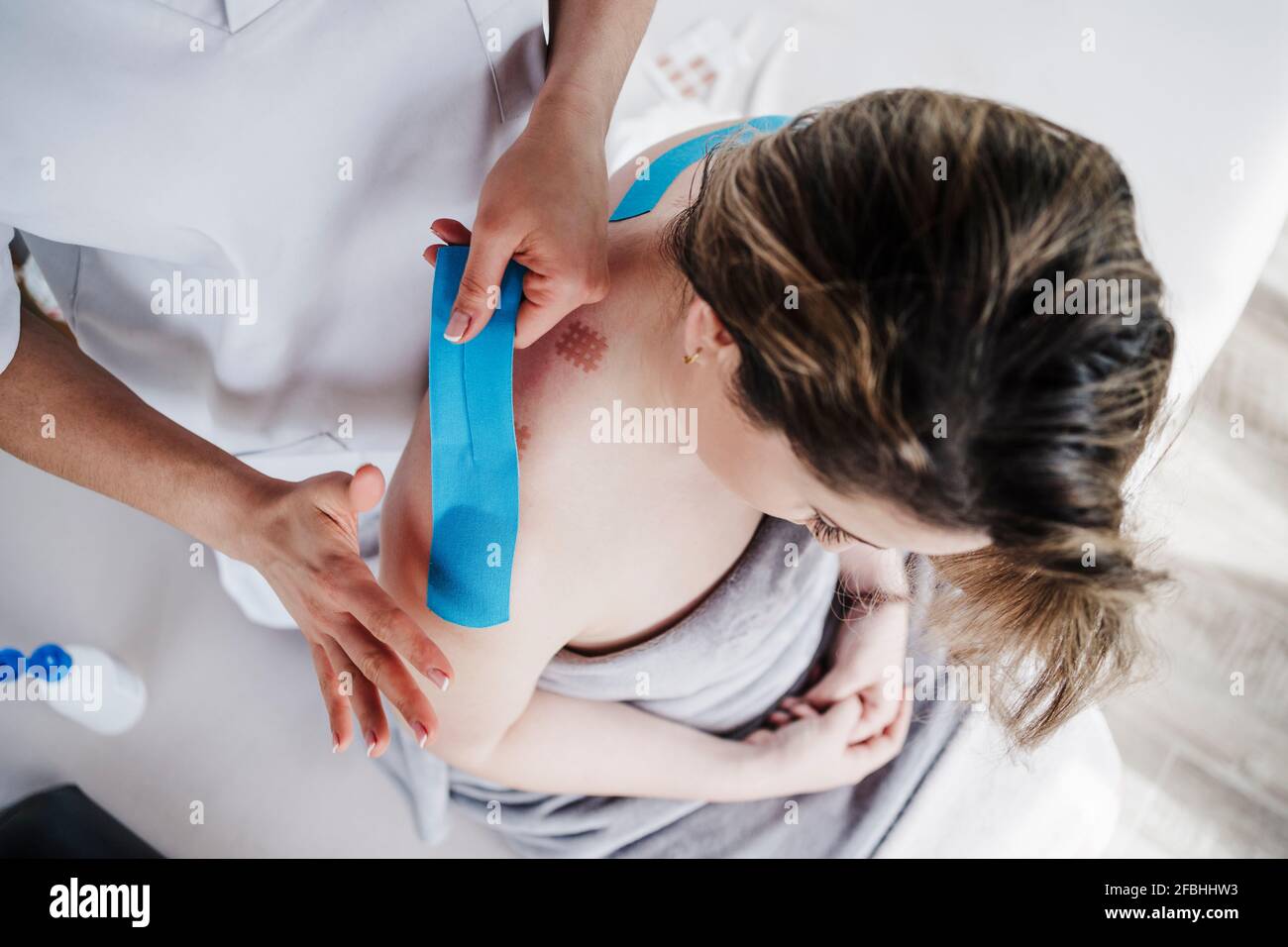 Physiotherapeutin klebt elastisches therapeutisches Klebeband an der Schulter des Patienten In der Klinik Stockfoto