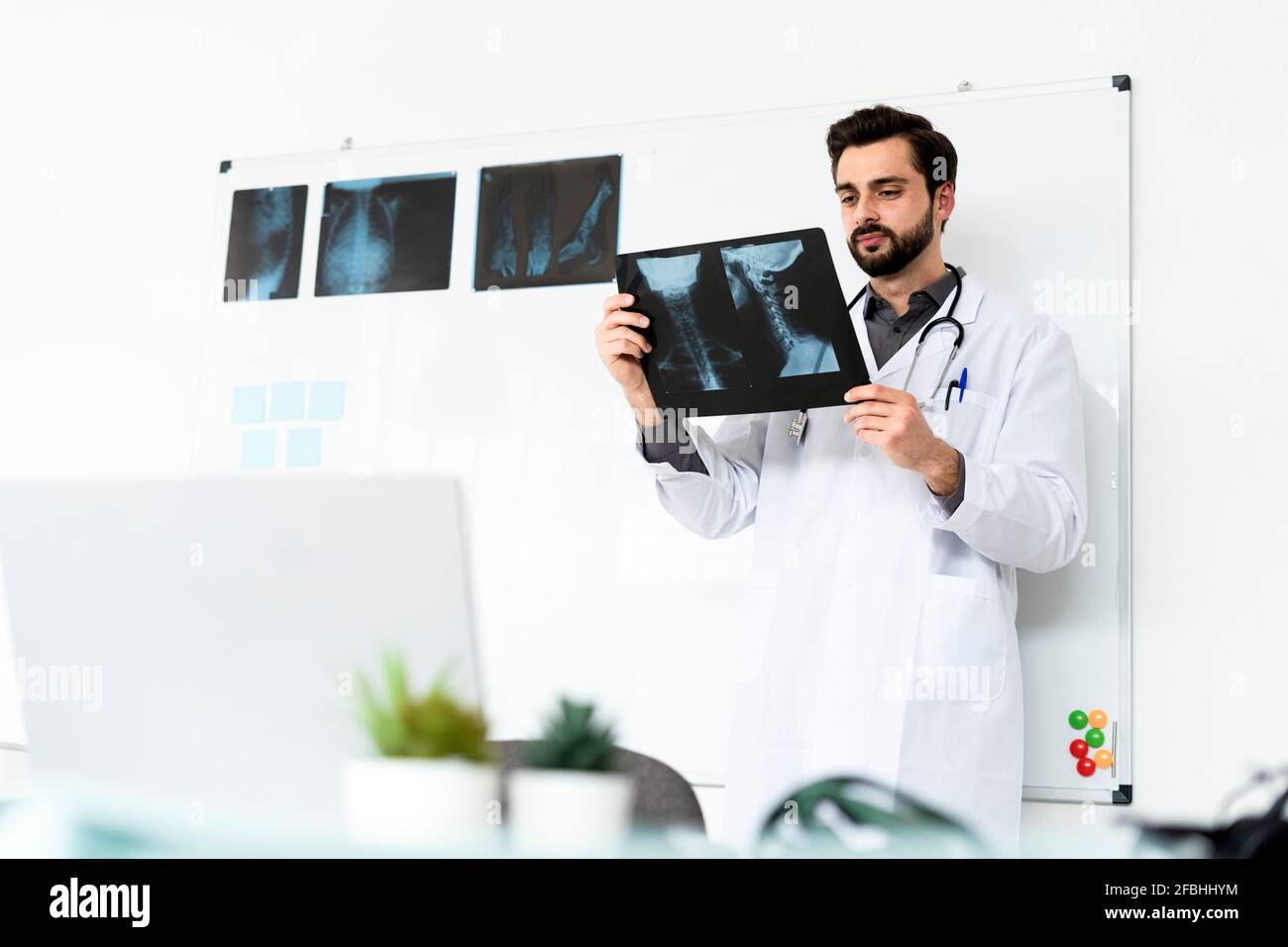 Männlicher Mitarbeiter im Gesundheitswesen, der Röntgenaufnahmen analysiert, während er vor dem steht Whiteboard im Krankenhaus Stockfoto