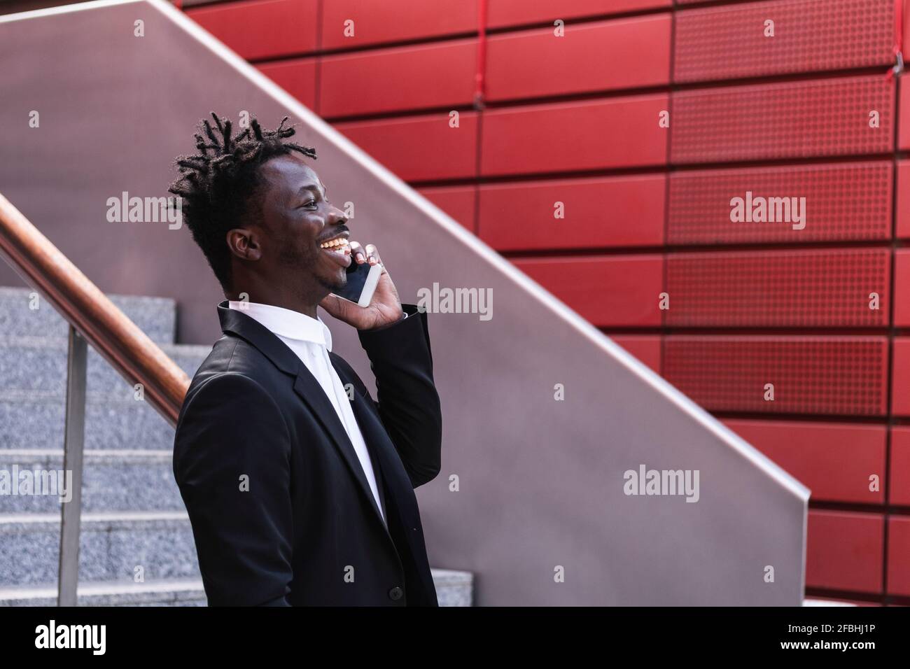 Fröhlicher Geschäftsmann, der Schritt für Schritt auf dem Mobiltelefon spricht Stockfoto
