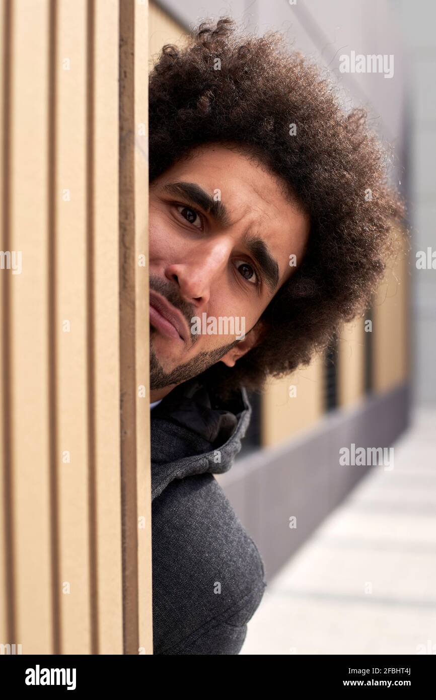 Verwirrter Afro-Mann, der sich hinter der Wand versteckt Stockfoto