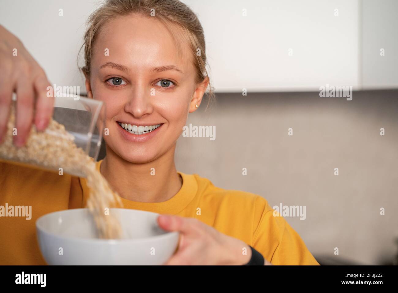 Junge Frau, die zu Hause Essen in eine Schüssel gießt Stockfoto