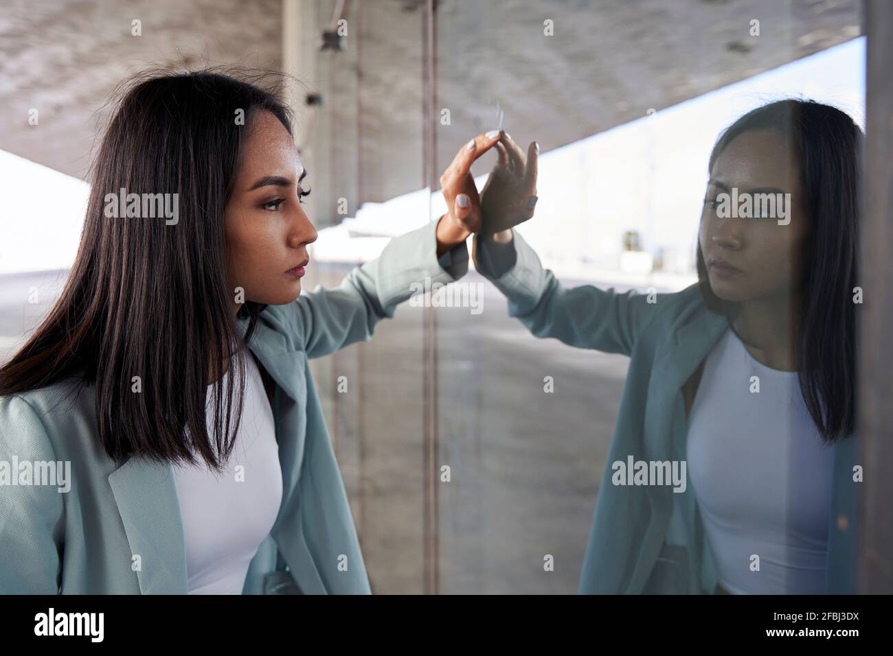 Schöne Geschäftsfrau, die auf Selbstreflexion an der Glaswand schaut Stockfoto