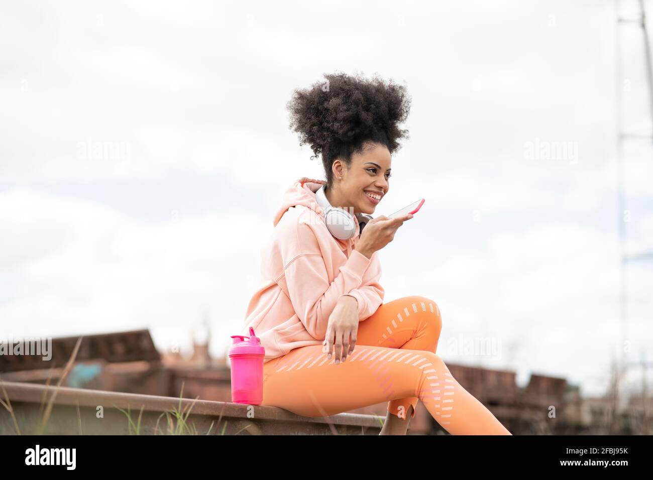 Frau, die während des Sitzens Sprachnachrichten über das Smartphone sendet Eisenbahnstrecke im Rangierbahnhof Stockfoto