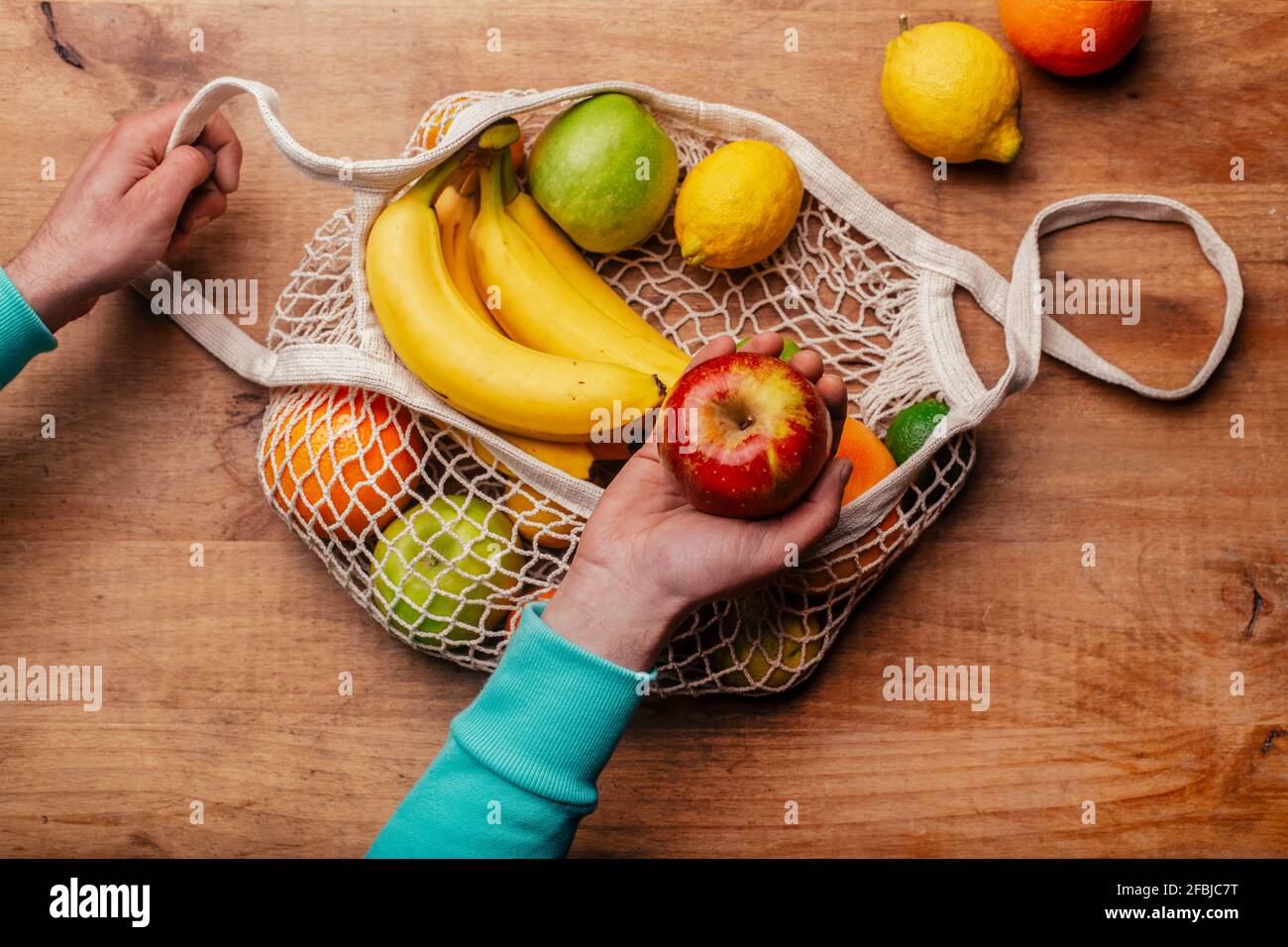 Wiederverwendbarer Baumwoll-Mesh-Beutel mit frischem Obst und Hand Mann mit reifen Äpfeln Stockfoto