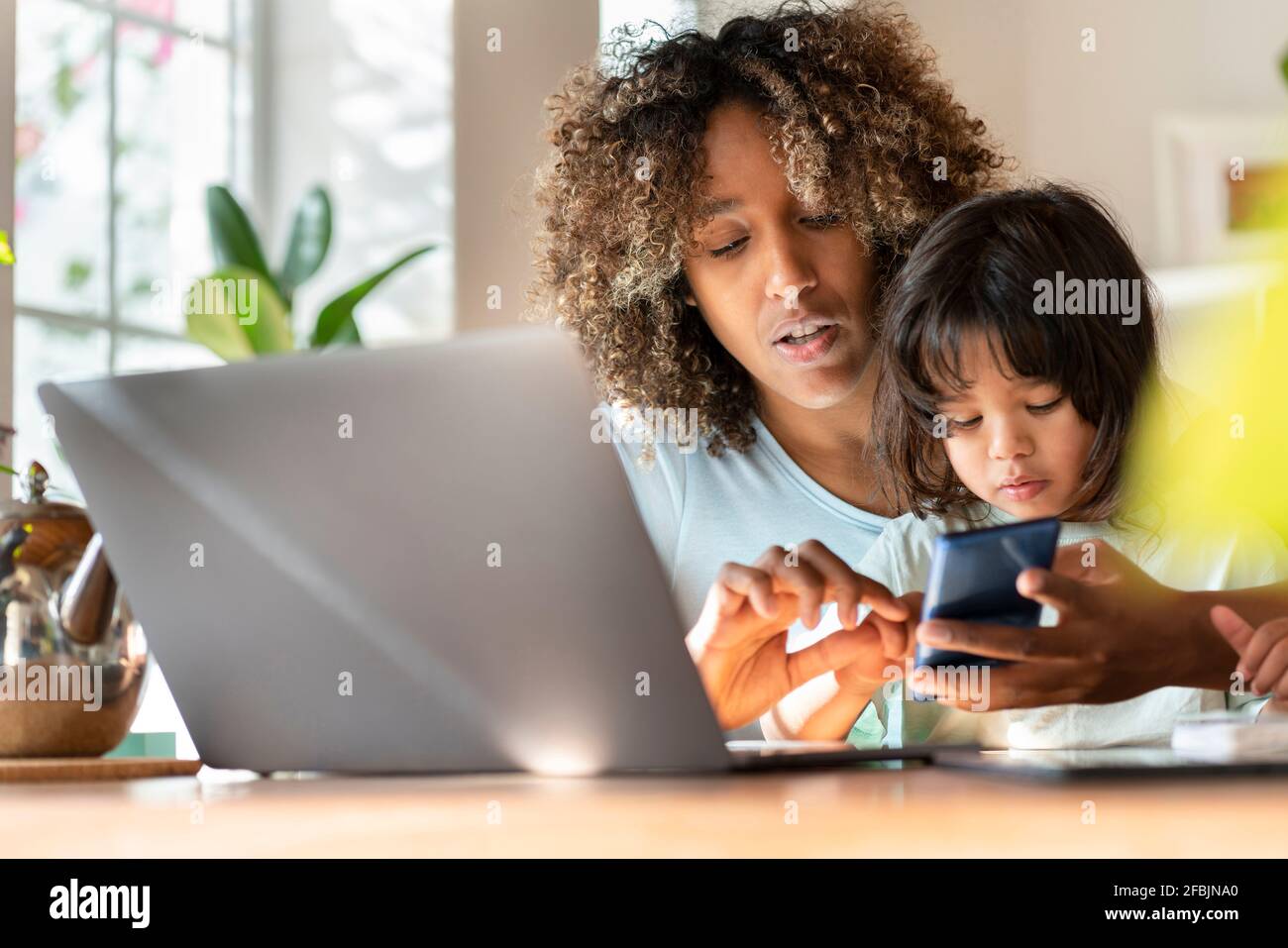 Mutter Multitasking während der Arbeit auf dem Smartphone mit Tochter in Heimbüro Stockfoto