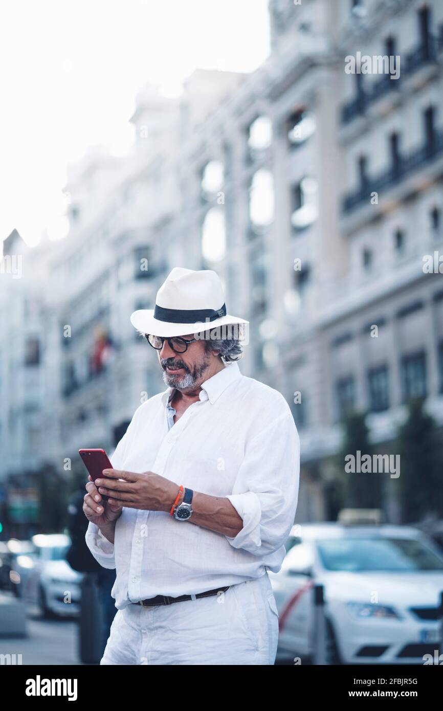 Älterer Mann mit weißer Kleidung und Hut mit Smartphone In der Straße von Madrid Stockfoto
