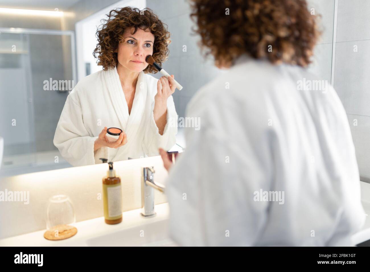 Schöne Frau, die im Badezimmer Puder aus Schminkpinsel aufgibt Stockfoto