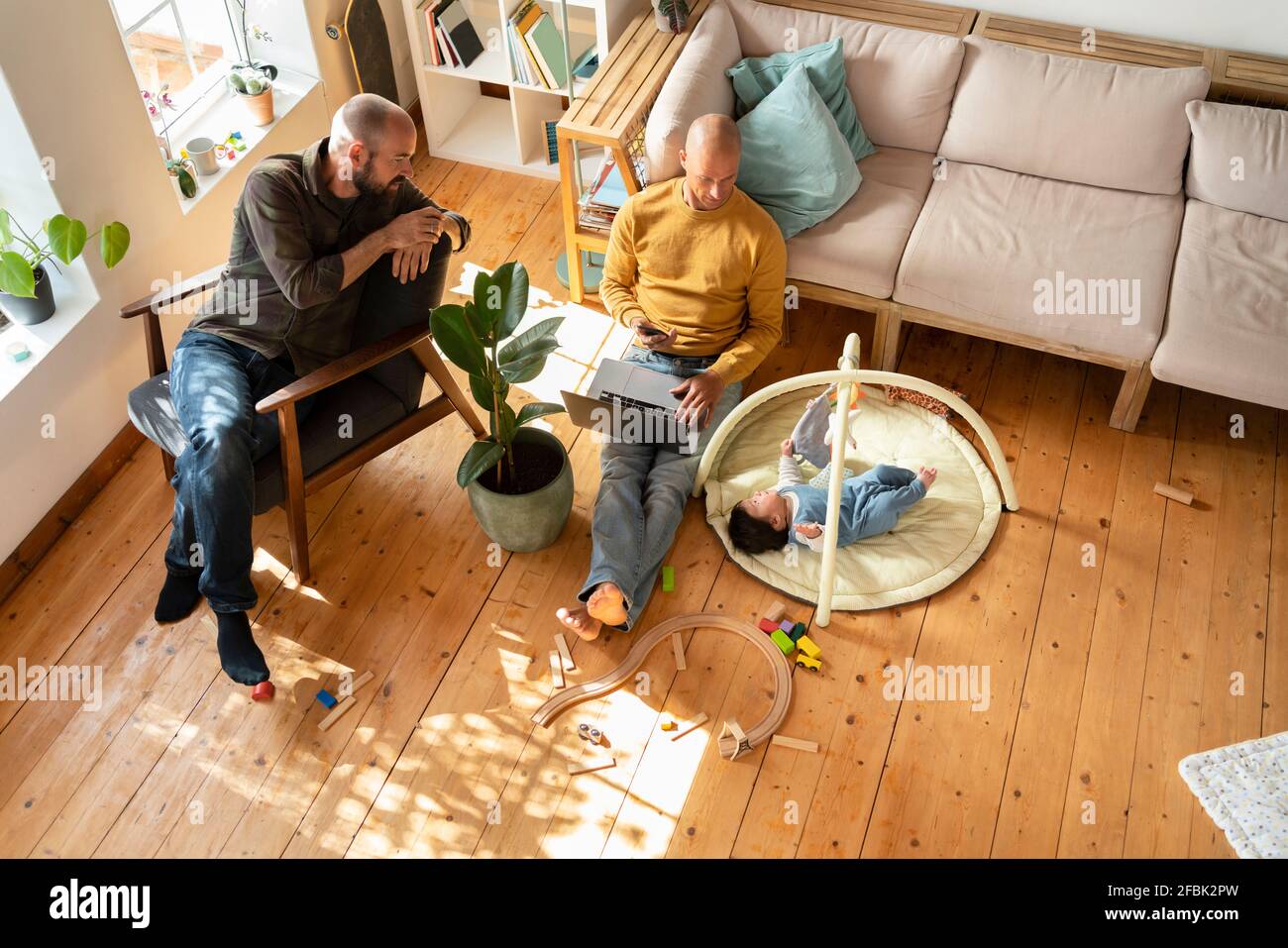 Zwei Männer, die auf dem Boden beim Spielen von Baby Girl zuschauen Wohnzimmer Stockfoto