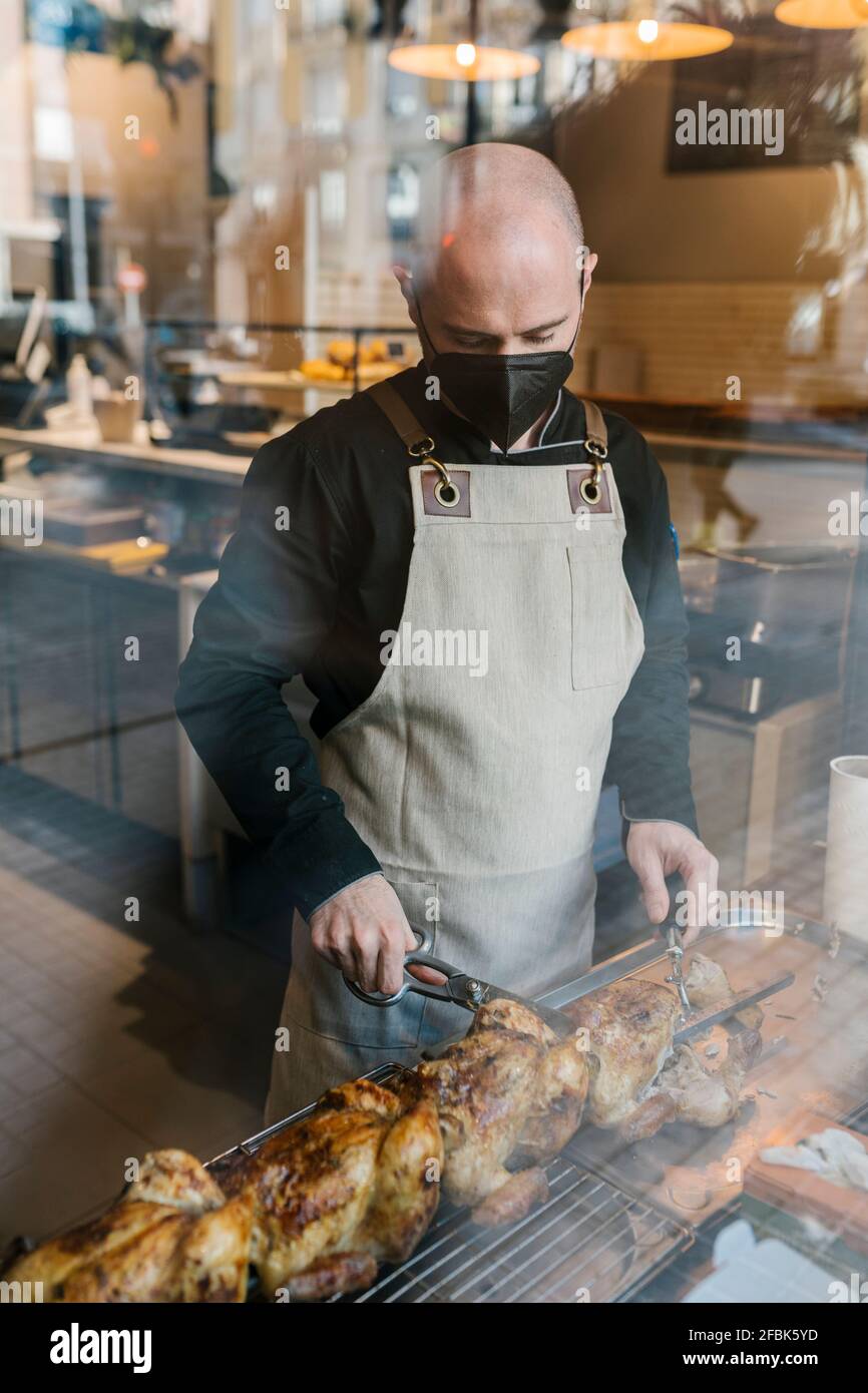 Der Chefkoch schneidet im Restaurant gebratenes Hähnchen, das durch das Glas gesehen wird Küche Stockfoto