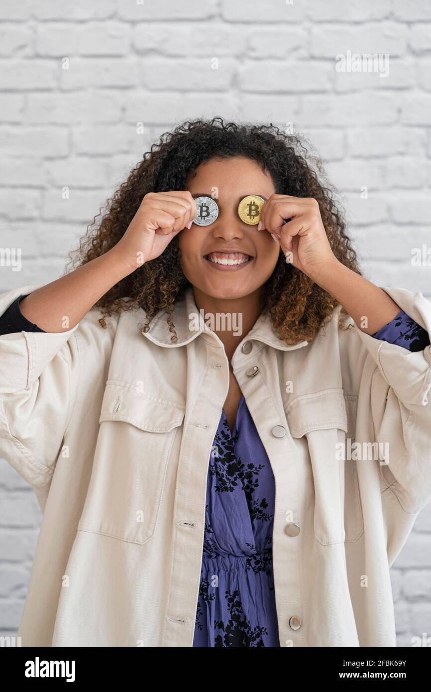 Lächelnde Frau, die Bitcoins vor den Augen hält Stockfoto
