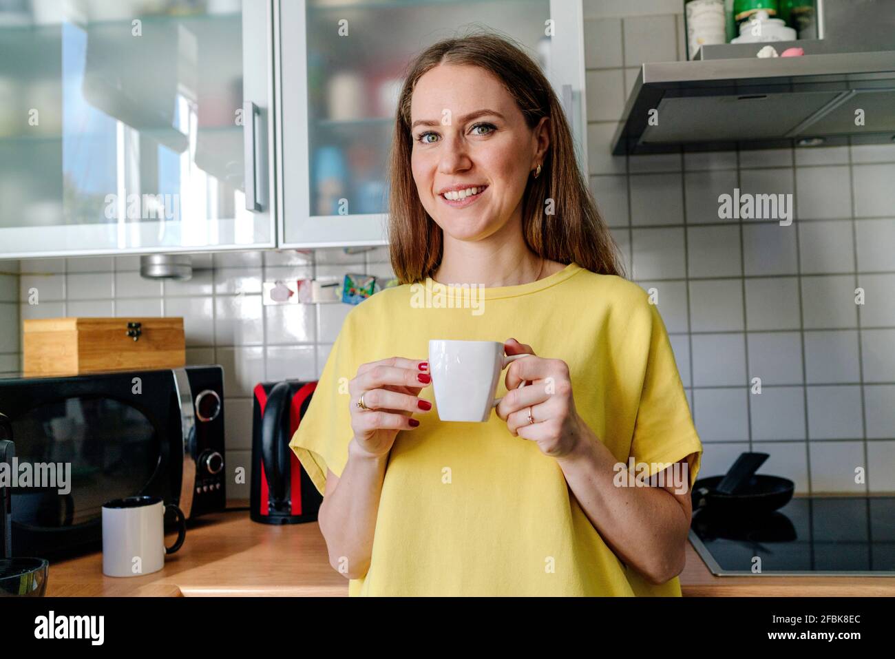 Lächelnde, braune Frau mit Kaffeetasse in der Küche Zu Hause Stockfoto