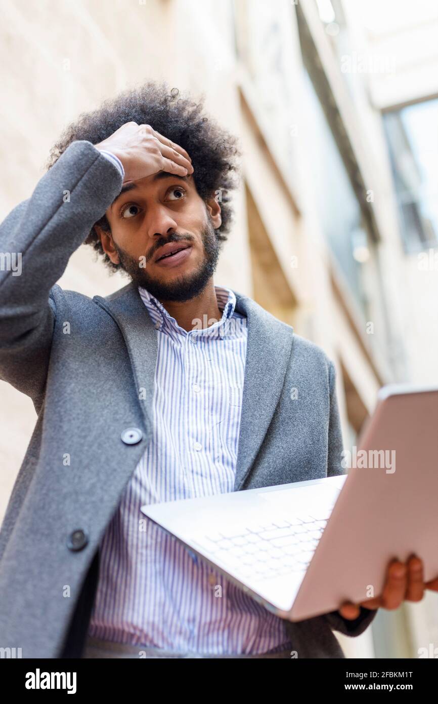 Enttäuschter männlicher Unternehmer mit Laptop, während er vor dem Gebäude stand Stockfoto