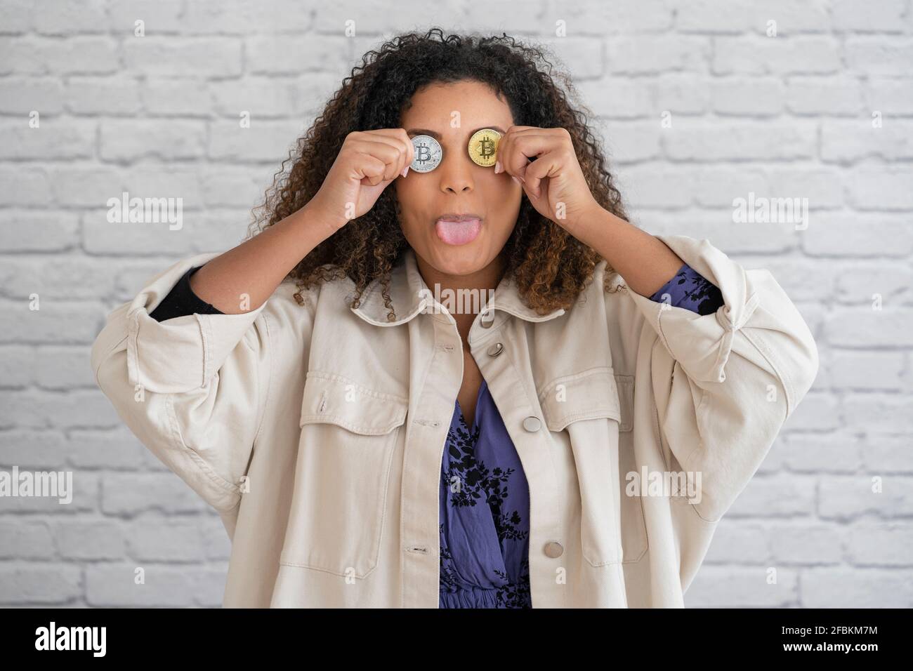 Verspielte Frau, die die Zunge herausstreckt und die Augen mit Bitcoins bedeckt Stockfoto