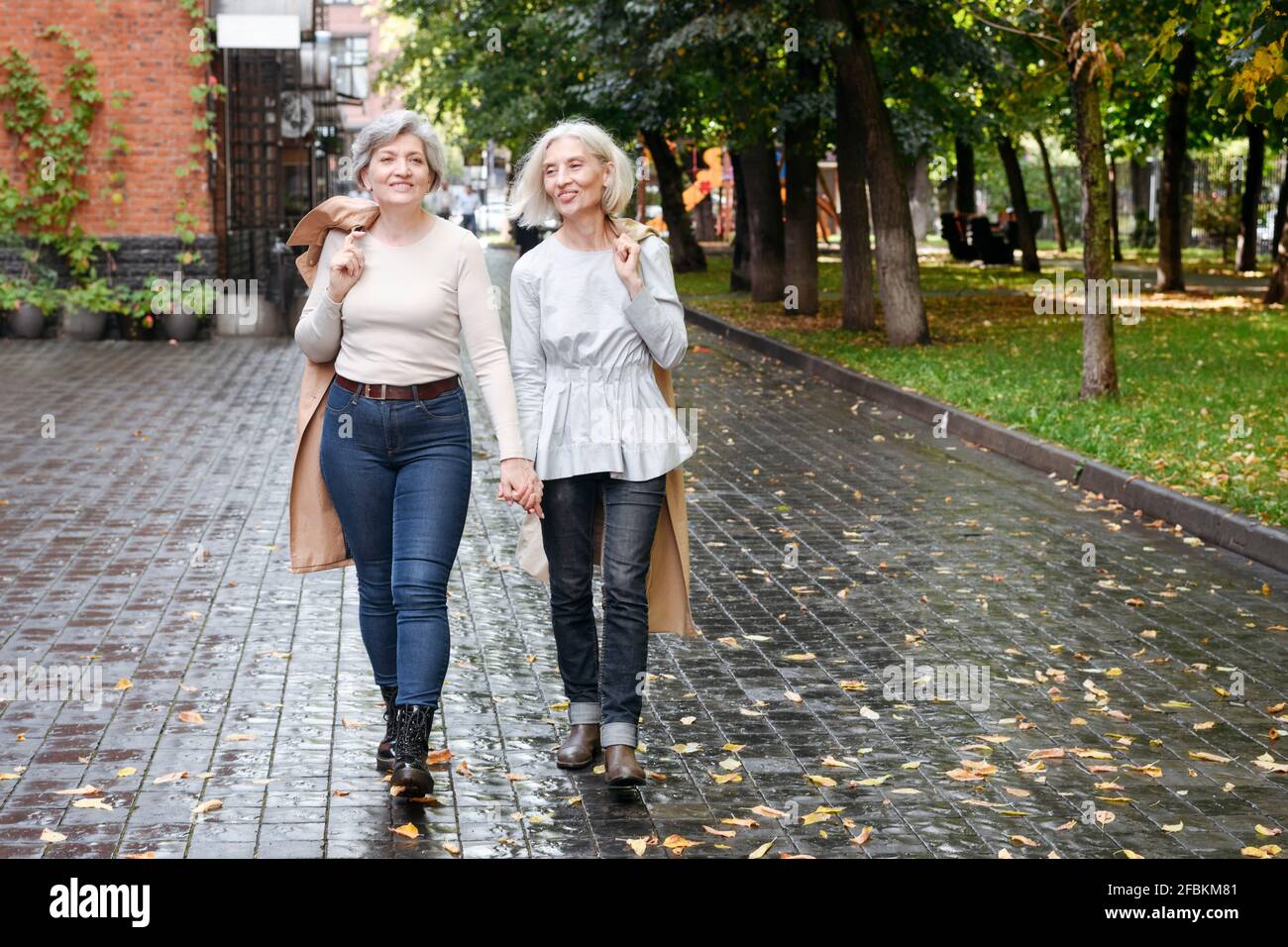 Lächelnde Freundinnen, die im Herbst auf einem nassen Fußweg spazieren Stockfoto