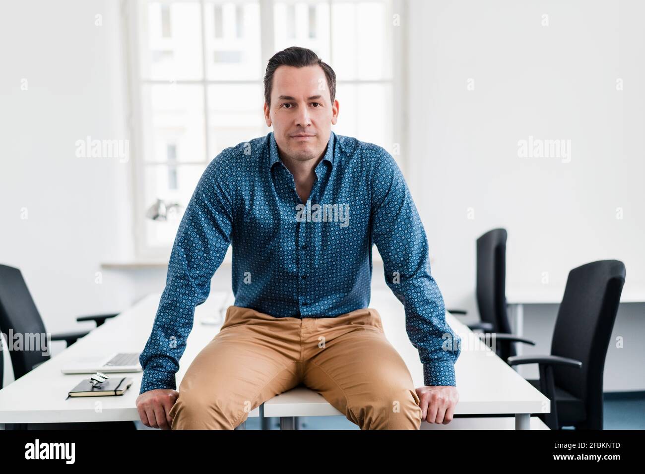 Männlicher Profi, der am Arbeitsplatz auf dem Schreibtisch sitzt Stockfoto
