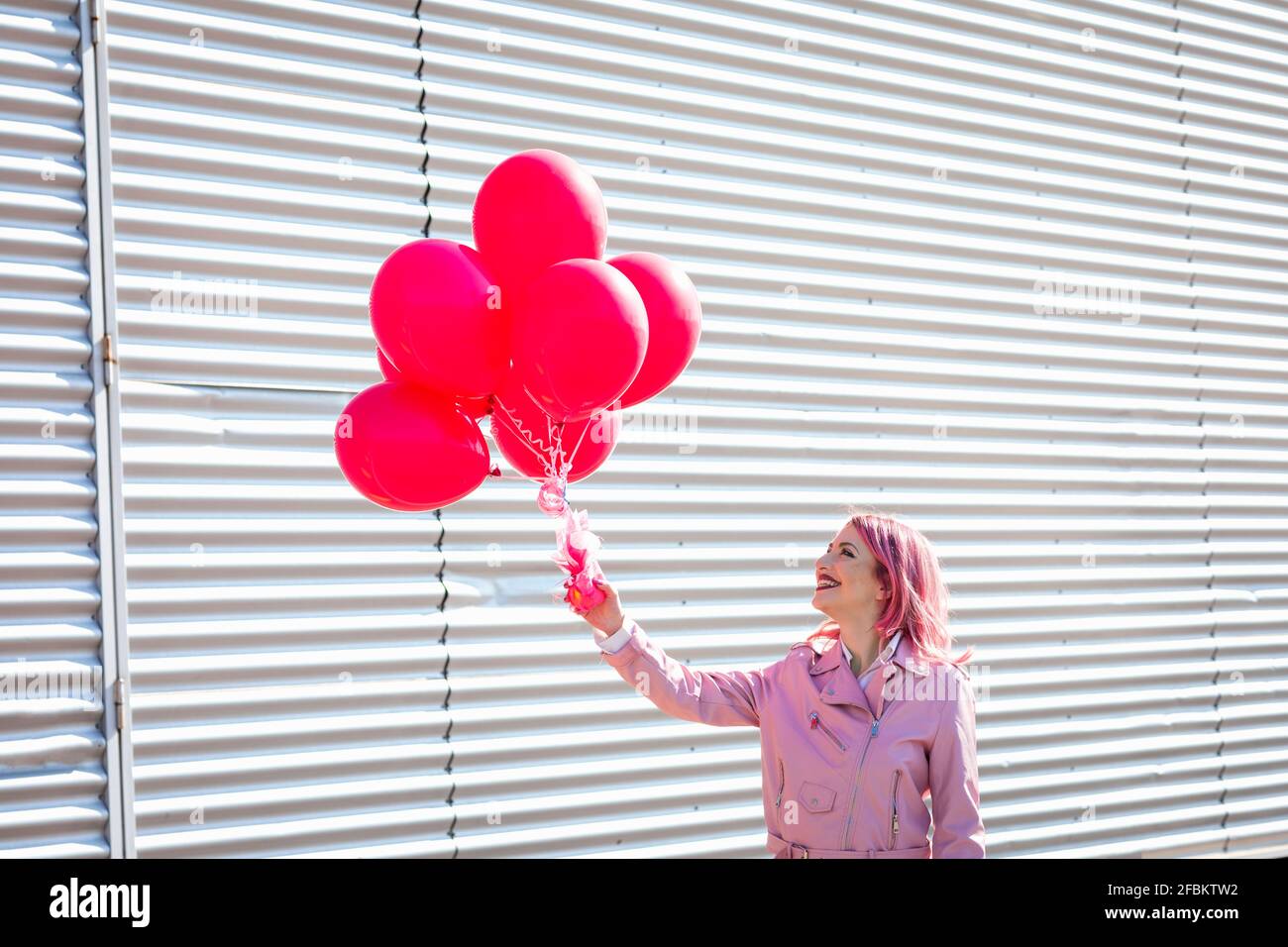 Glückliche Frau hält rosa Ballons an der Metallwand während der Sonne Tag Stockfoto