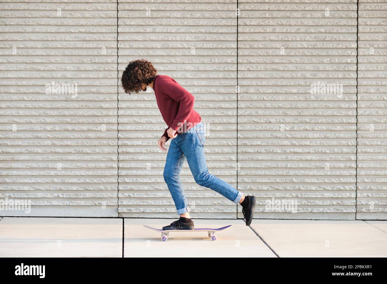 Curly haired man Skateboarding an der Wand Stockfoto