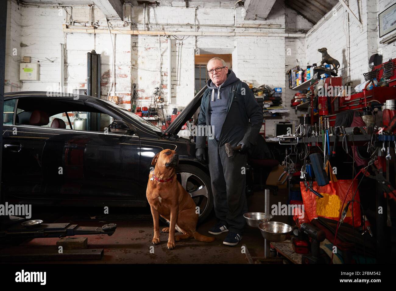 Älterer männlicher Reparaturmann, der neben dem Hund in der Garage steht Stockfoto