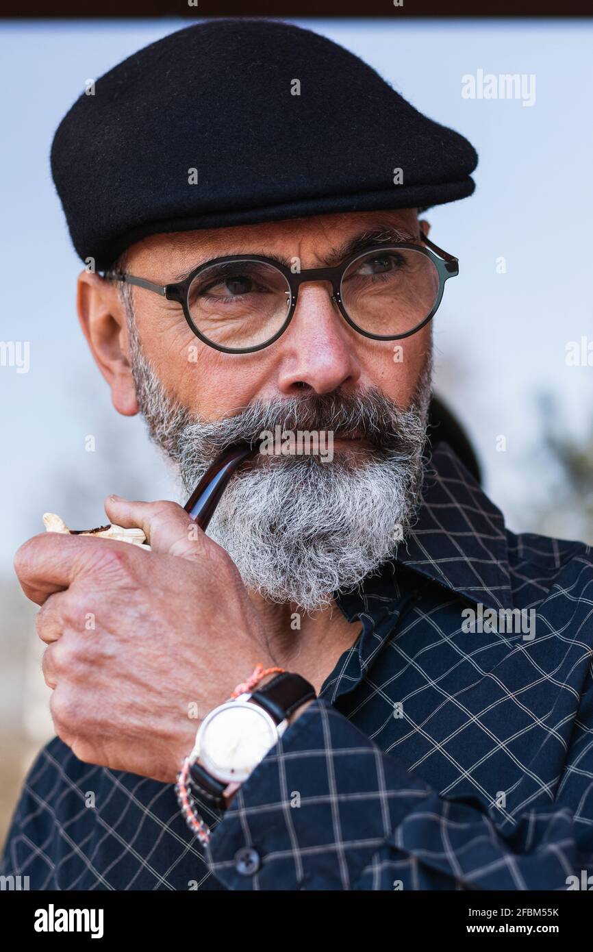 Bärtiger Mann mit flachem Hut, der beim Rauchen wegschaute Rohr Stockfoto