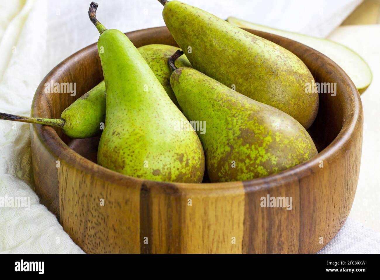 Frische grüne Bio-Birnen reifen in der runden Holzschale auf hellem Hintergrund in der Küche. Stockfoto