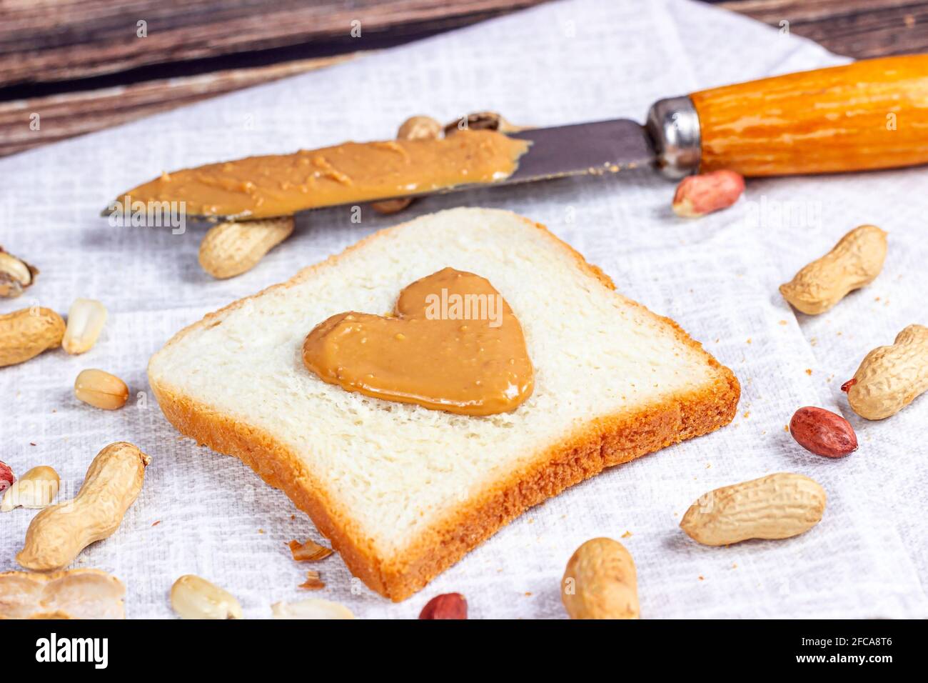 Hausgemachtes Toast zum Frühstück mit frischer, knuspriger, herzförmiger Erdnussbutter und Nüssen auf hellem Textilhintergrund. Stockfoto