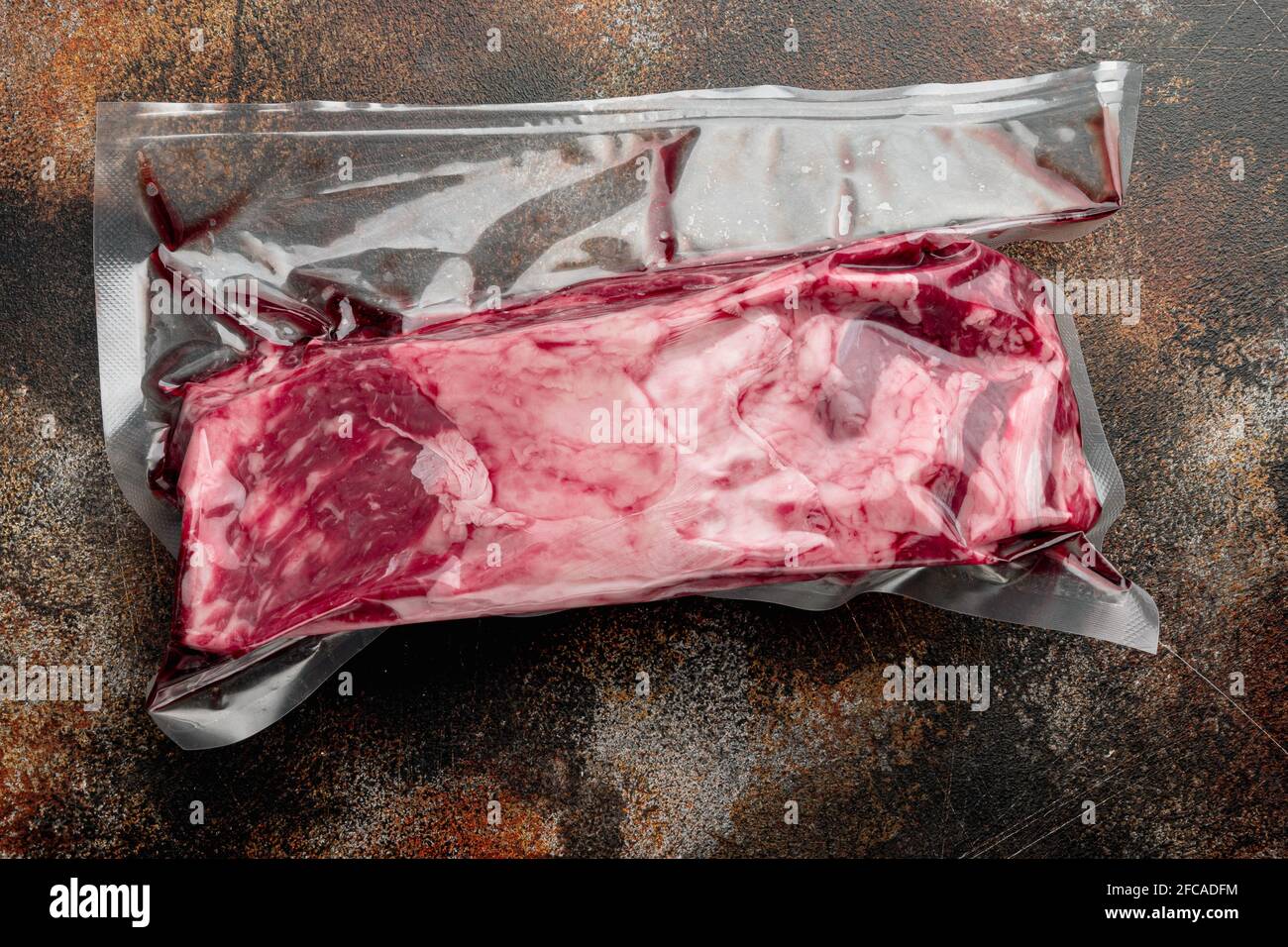 RAW Rib Eye Beef Steak in Vakuumverpackung geschnitten, auf altem dunklen rustikalen Hintergrund, Draufsicht flach liegend, mit Platz für Text Stockfoto