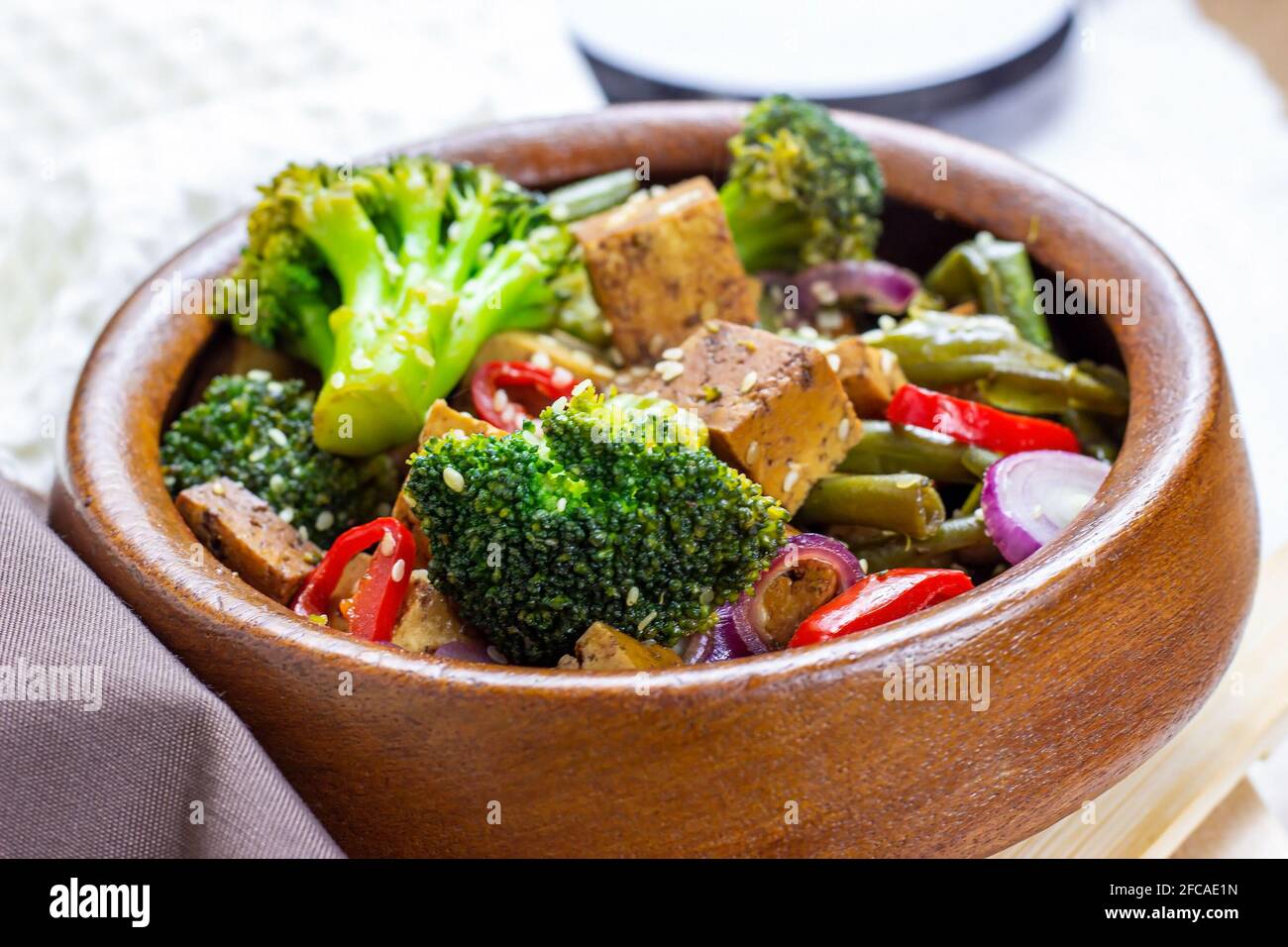 Hausgemachter vegetarischer gebratener Tofu mit Gemüse (Brokkoli, Pfeffer, Zwiebeln und grüne Bohnen) in der Holzschüssel. Stockfoto