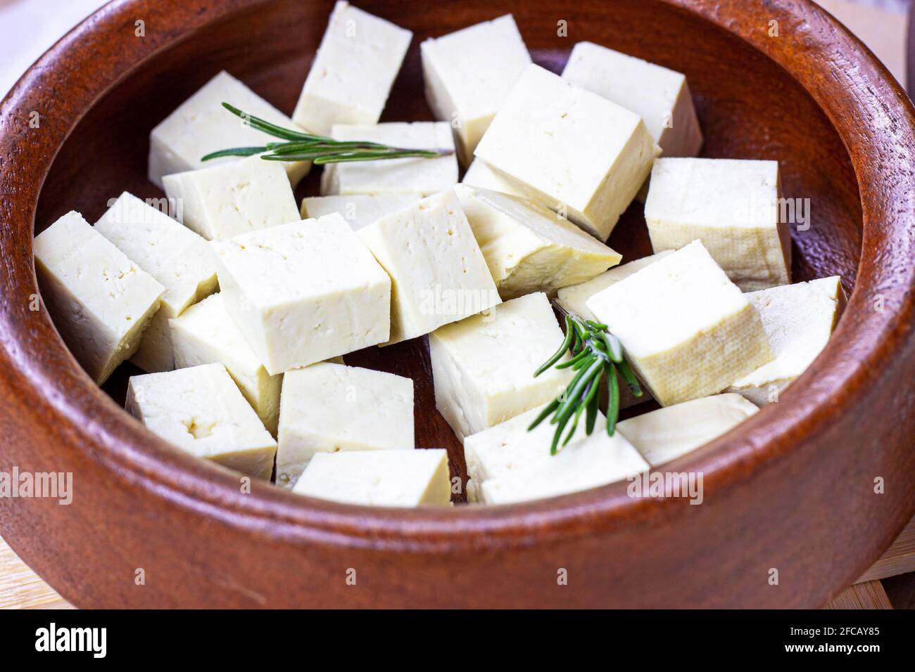 Rohe vegetarische Bio-Tofu-Würfel in runder Holzschüssel mit frischem Rosmarin. Stockfoto