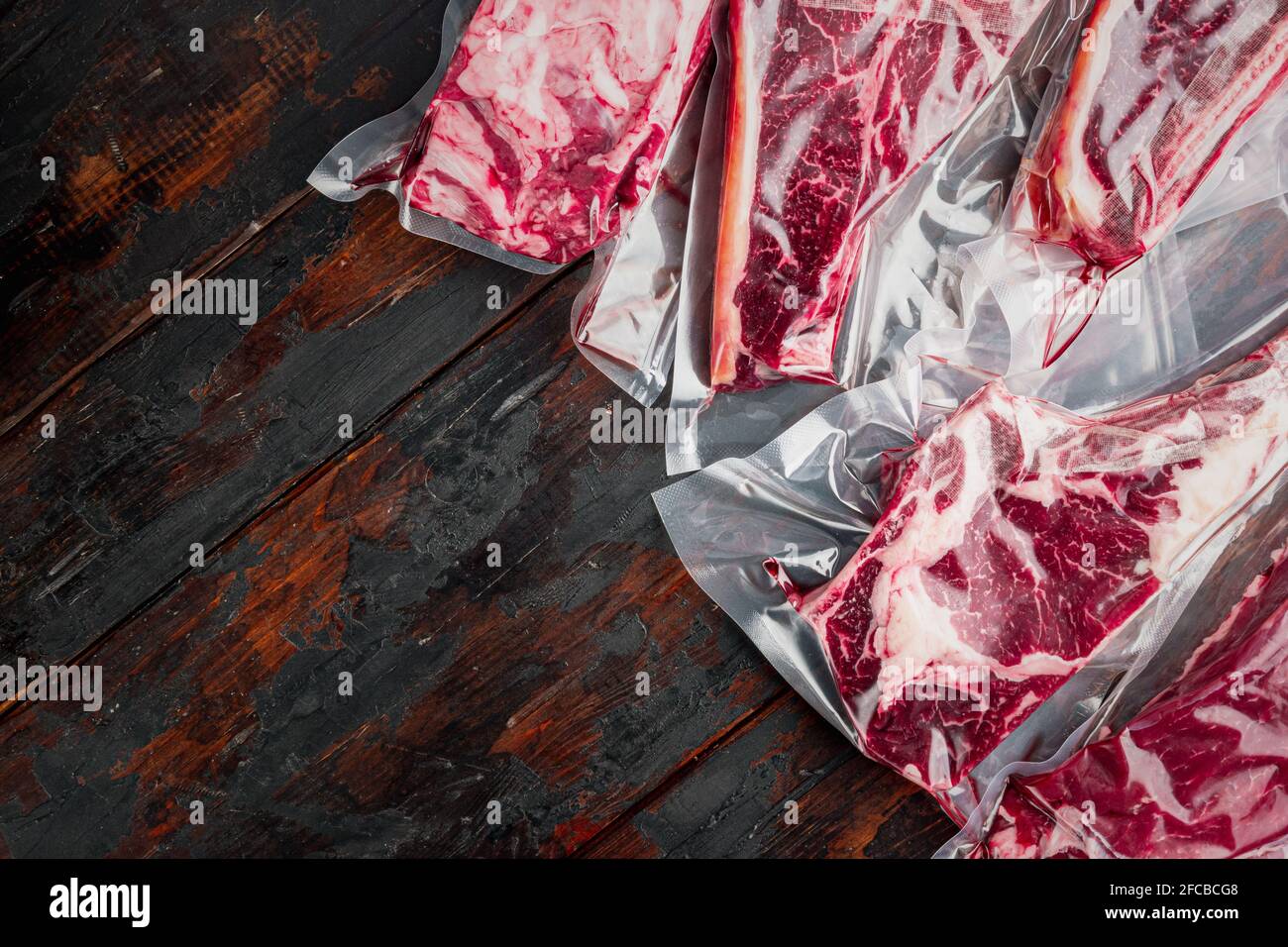 Rindersteak vakuumversiegelt, bereit für Sous-Vide-Garset, Tomahawk, T-Bone, Clubsteak, Rib-Eye- und Filet-Schnitte, auf altem dunklen Holztisch-Backgrou Stockfoto