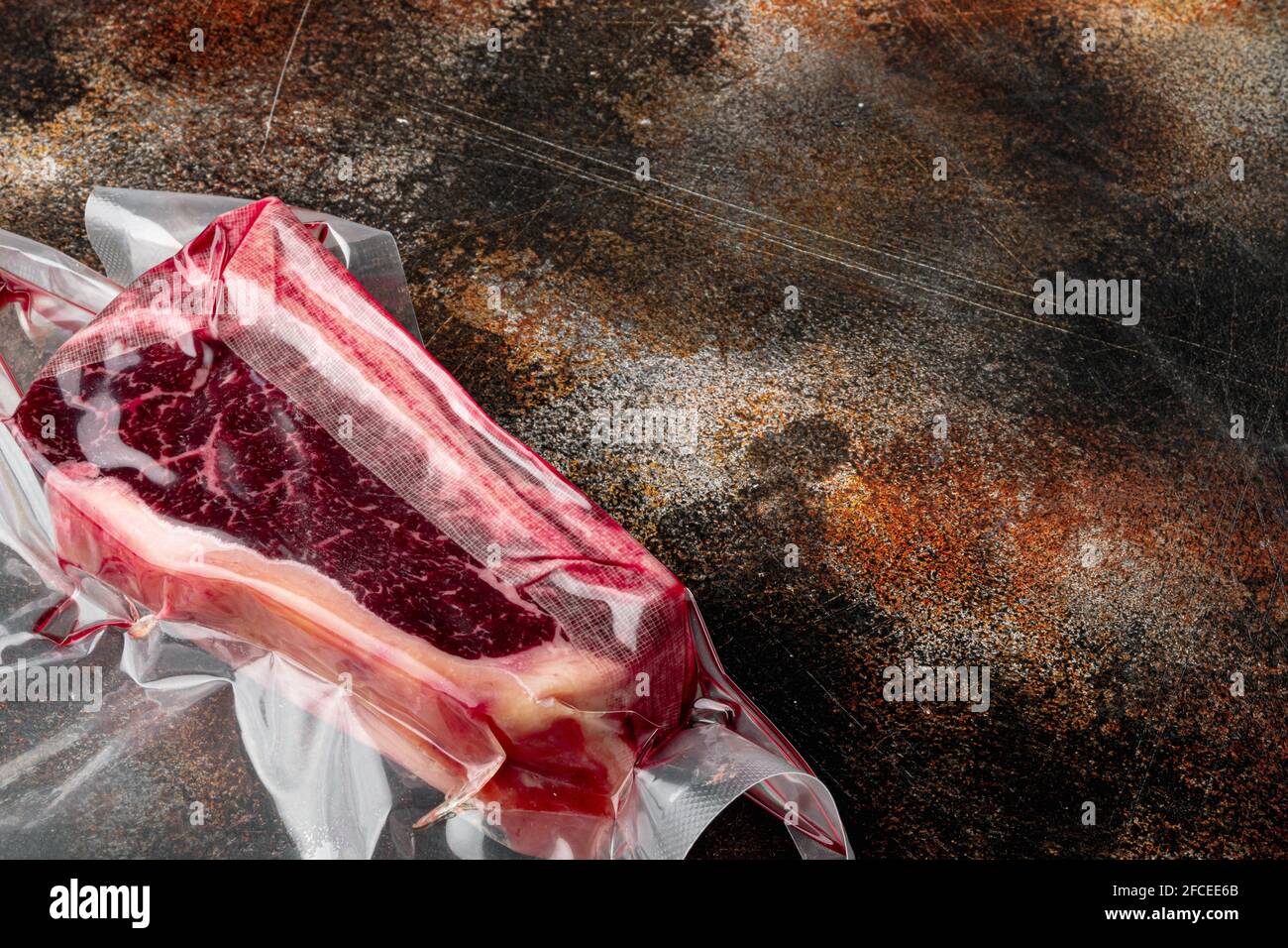 Trocken gereiftes Rindfleisch, marmoriertes Fleisch, rohes, frisches Clubbeefsteak in Plastikpackung, auf altem dunklen, rustikalen Hintergrund, mit Platz für Text Stockfoto