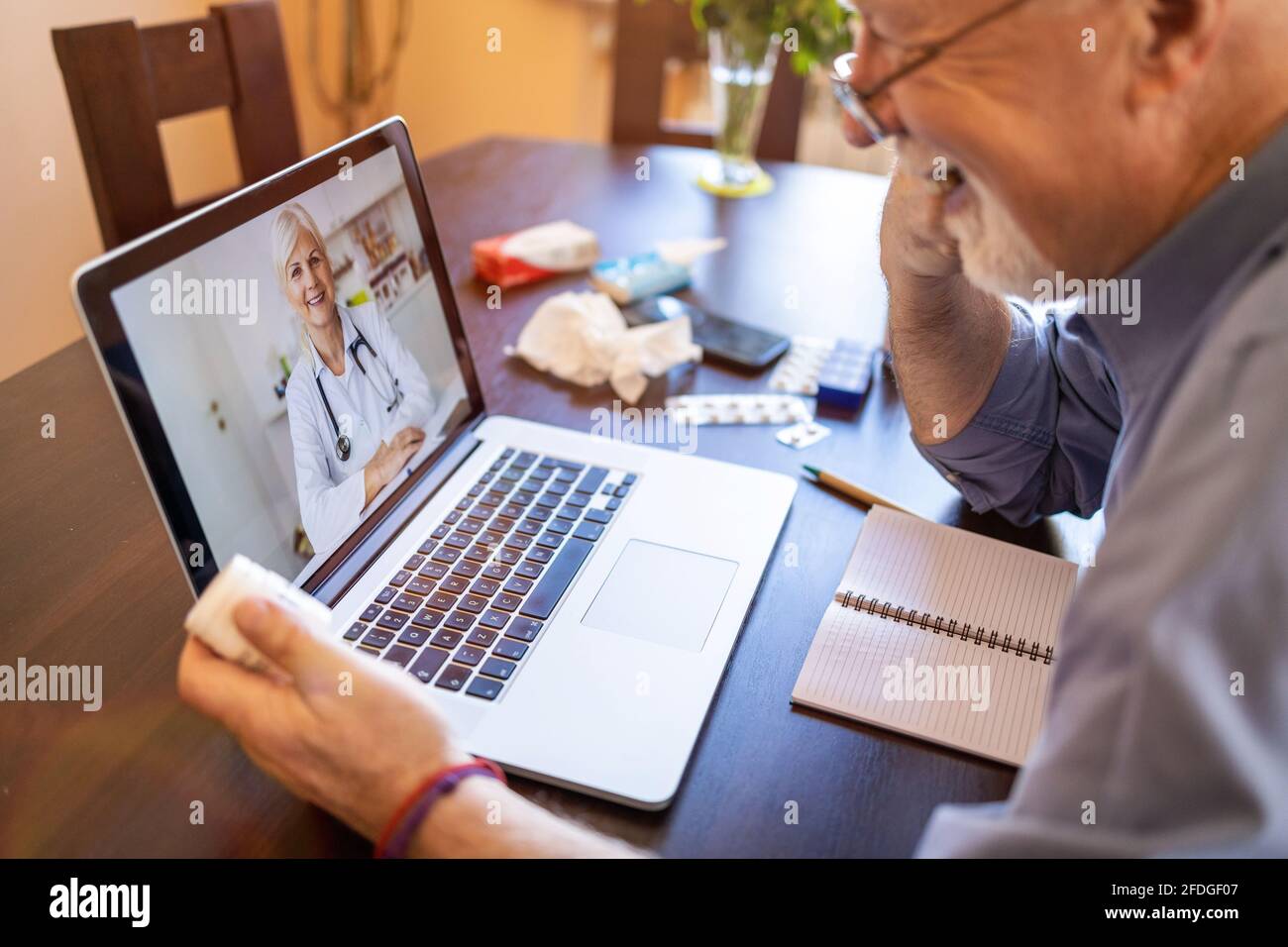 Ein älterer Mann, der sich mit einem Arzt auf seinem Laptop beraten hat Stockfoto