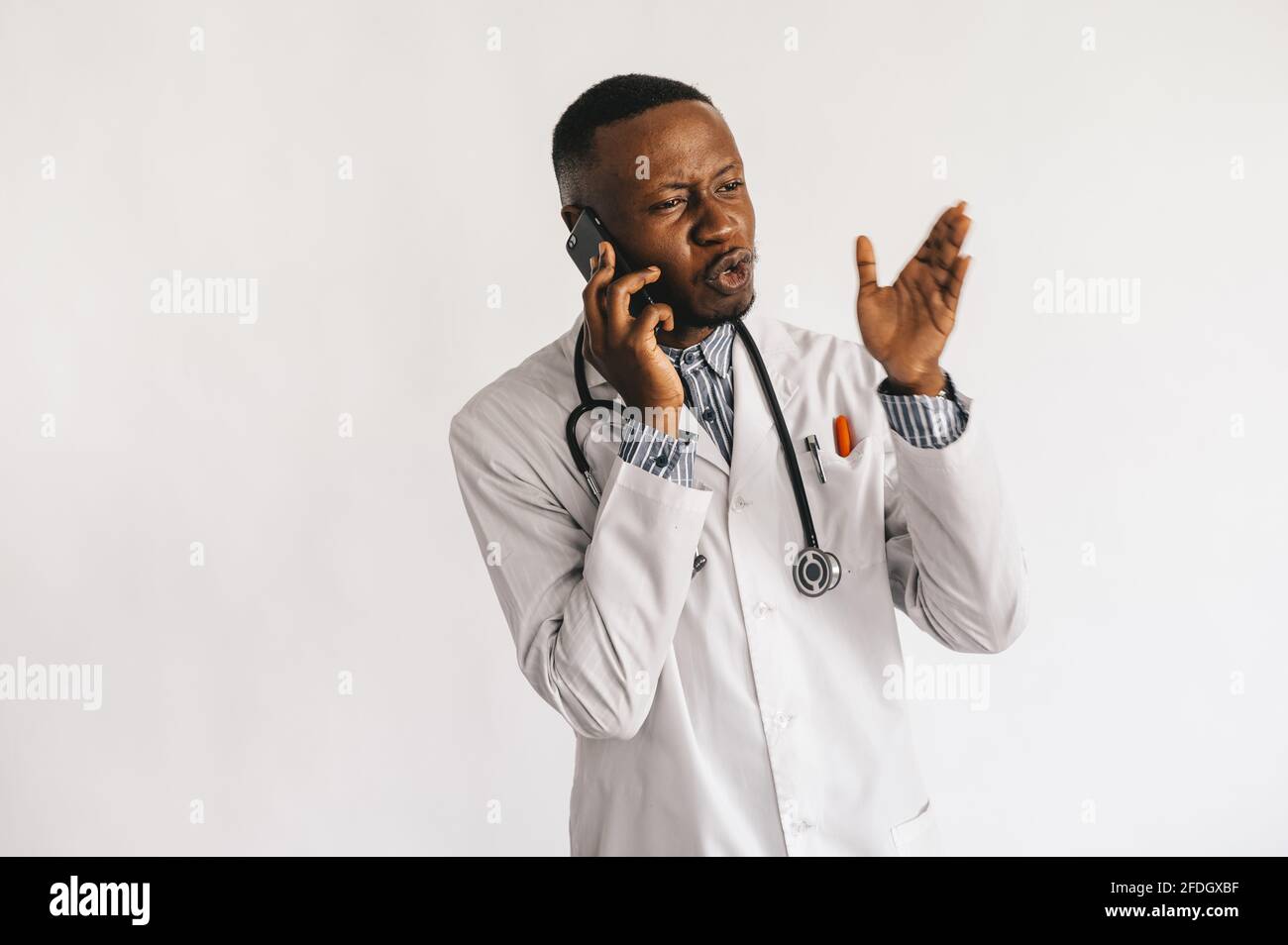 Ein afroamerikanischer schwarzer junger Arzt in einem weißen Mantel spricht am Telefon. Isoliert Stockfoto