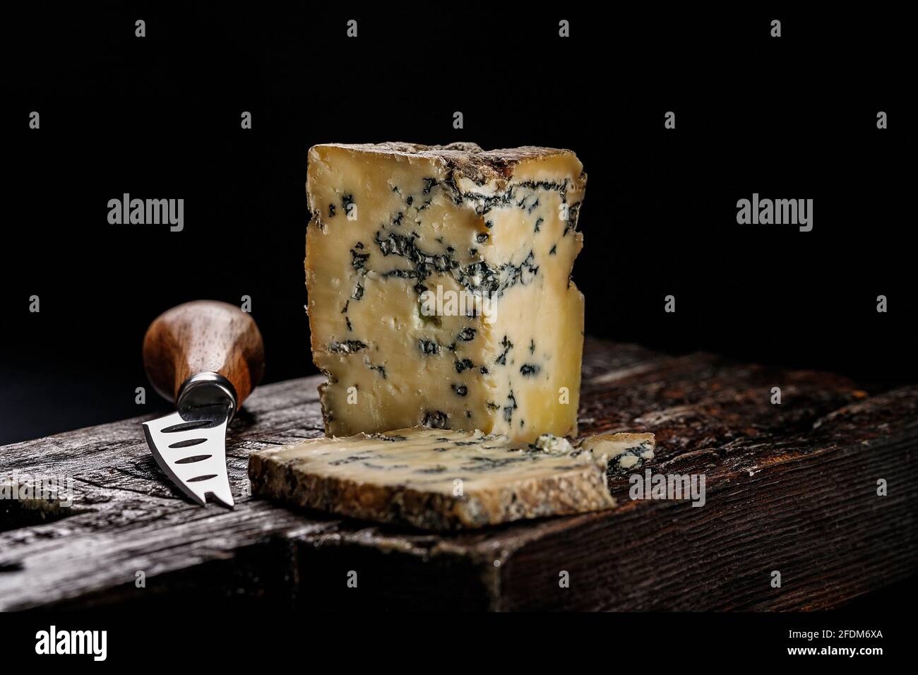 Halbweicher Käse mit Schimmel aus Kuhmilch. Der König der blauen Käsesorten ist Stilton. Stück Käse auf einem dunklen Holzbrett und Messer zum Schneiden von Chee Stockfoto