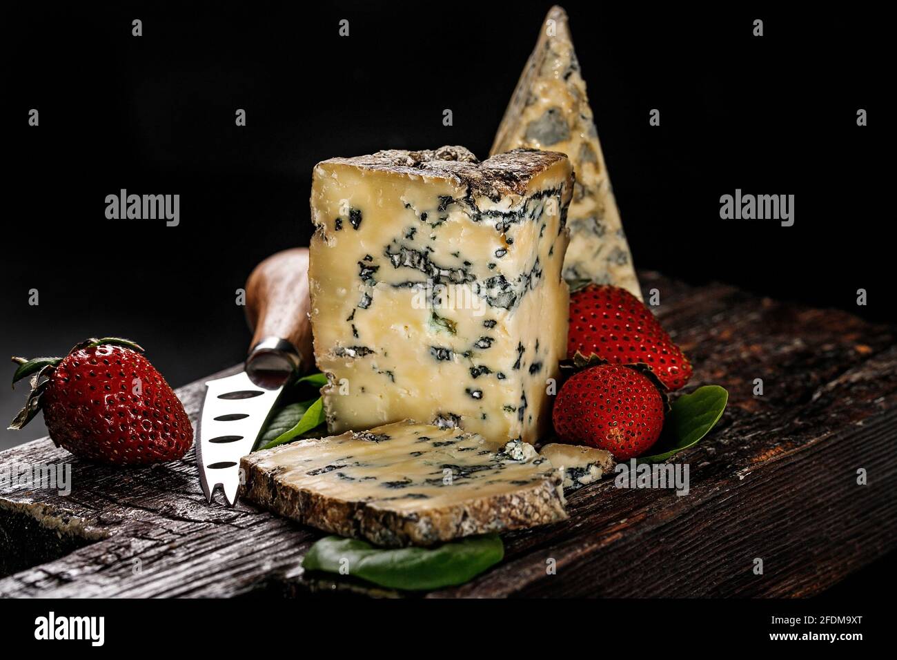 Halbweicher Käse mit Schimmel aus Kuhmilch. Der König der blauen Käsesorten ist Stilton. Ein Stück Käse und reife Erdbeeren auf einem dunklen Holzbrett und Stockfoto