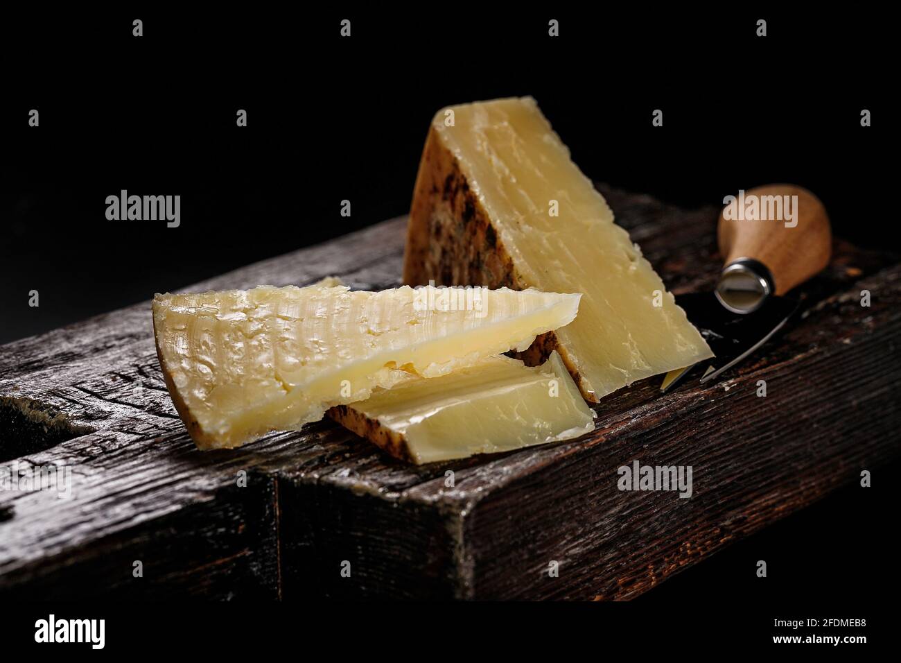 Nahaufnahme von Cheddar-Käse. Halbweicher, gereifter Kuhmilchkäse nach einem alten englischen Rezept. Stück Käse auf einem dunklen Holzbrett und Messer für Stockfoto