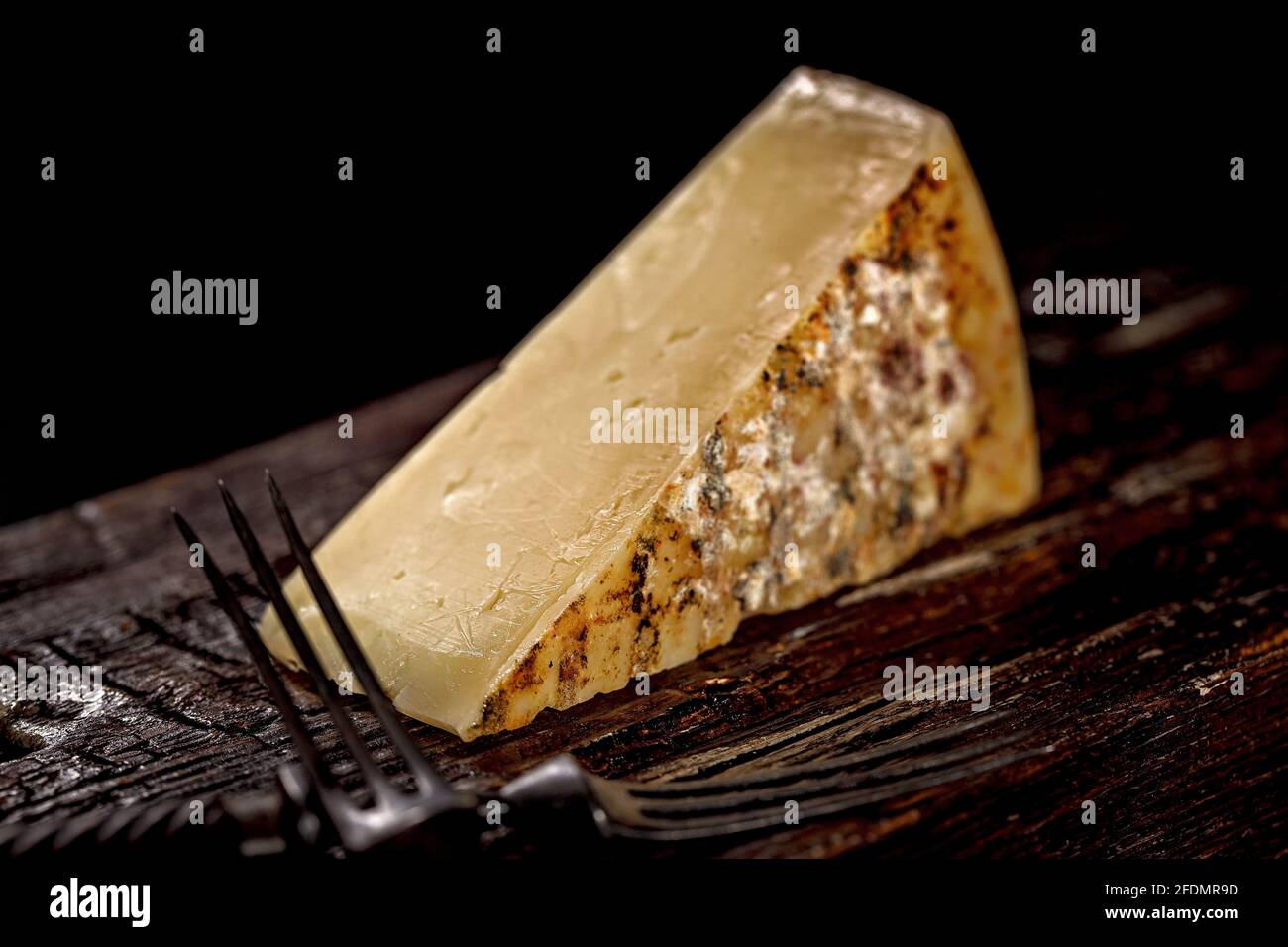 Nahaufnahme eines Stücks Cheddar-Käse. Gereiftem Käse aus Bauernmilch, ein altes englisches Rezept. Ein Stück Käse auf einem dunklen Holzbrett und ein Käse k Stockfoto