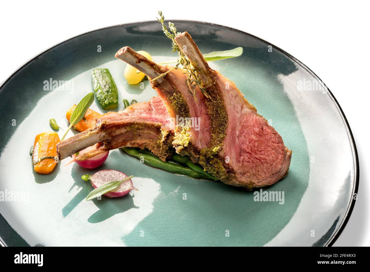 Verkrustete Lammrippen Schnitzel mit Knochen in grüner Schale mit Karotten, Radieschen und Zucchini, Nahaufnahme Stockfoto